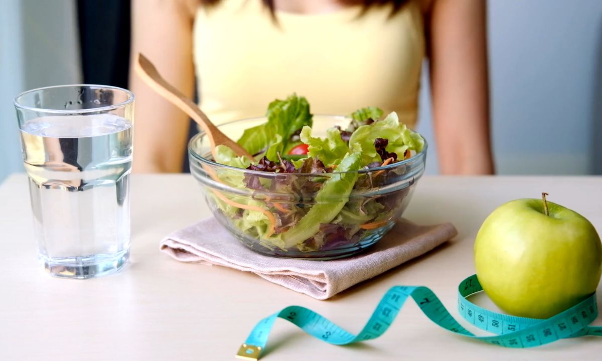 devojka na jednodevnom detoksu, ispred nje salata, jabuka, čaša vode i metar za merenje